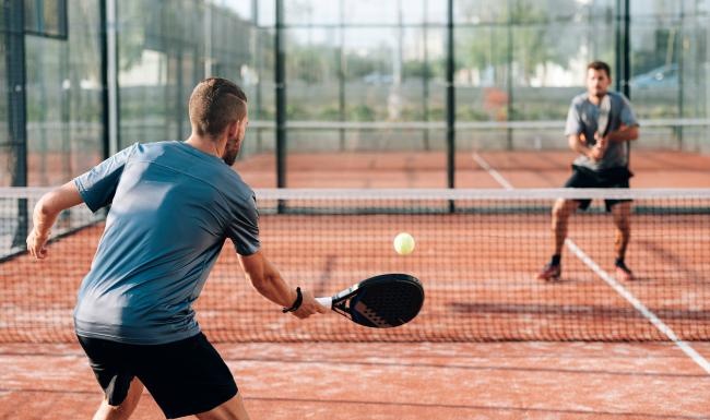 a person hitting a ball with a pickleball paddle to another person