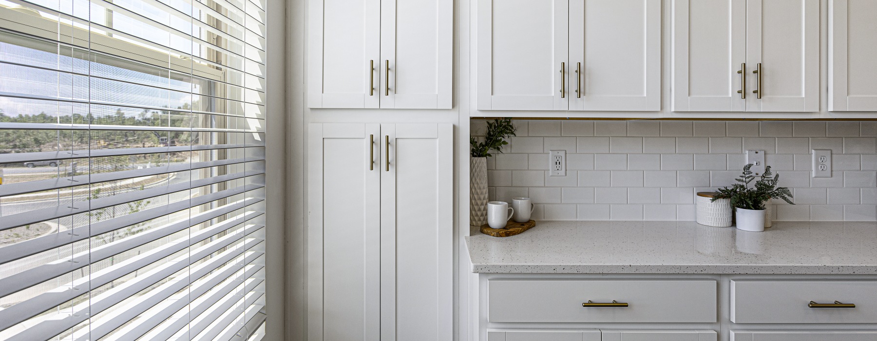 Model kitchen at Sunstone Grove Apartments in Waldorf, MD, featuring white cabinetry and large windows with blinds.